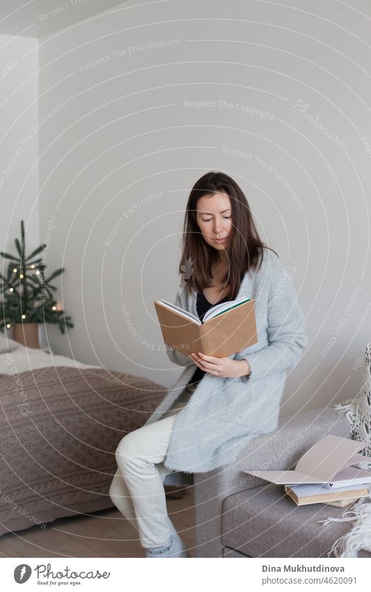 Frau sitzt auf einer Couch und liest ein Buch in einer gemütlichen Wohnung Appartement Person im Innenbereich sich[Akk] entspannen Sitzen heimwärts bequem lesen