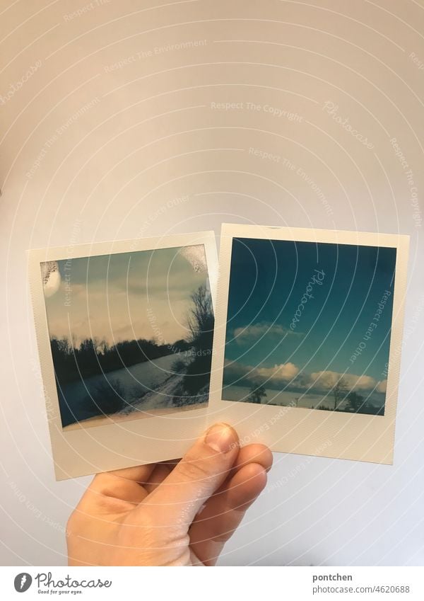 eine Hand hält zwei Polaroids vor eine weiße wand. stolz Fotos betrachten. polaroids fotos sofortbild fotografie landschaft inn fluß himmel wolken
