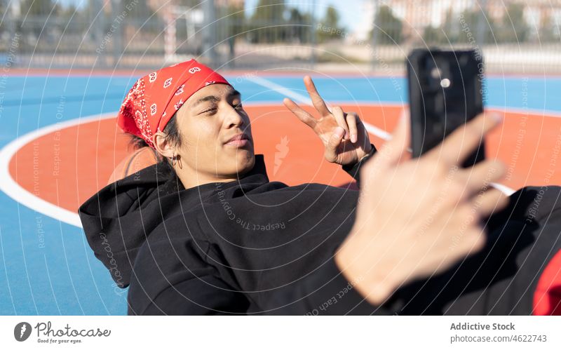 Asiatischer Mann, der ein Selfie auf dem Plauground macht Smartphone Selbstportrait v-Zeichen Spielplatz Sportpark Hobby Training Porträt asiatisch Zaun