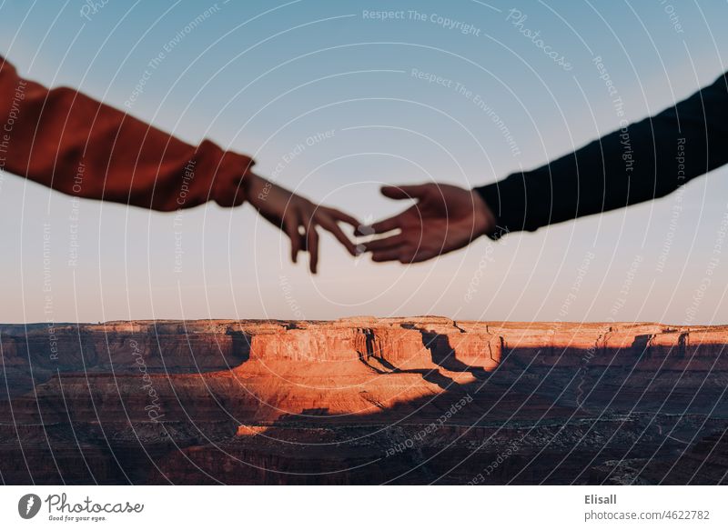 Ein Paar greift nach den Händen des anderen vor einem Canyon in der Wüste Paare erreichend hinausreichend Schlucht Canyons Western Sonnenaufgang Liebe abstützen