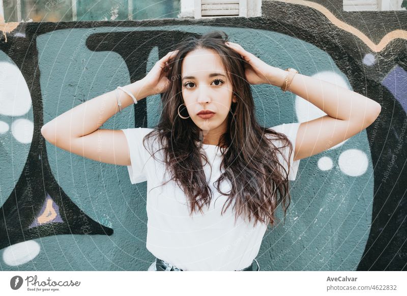 Porträt eines jungen arabisch-afrikanischen Mädchens mit ernster Hip-Hop-Haltung, das ernst in die Kamera schaut, auf einem weißen Hemd mit Graffiti-Hintergrund. Schönheit junge Straße Leben Straßenkünstler in der Stadt
