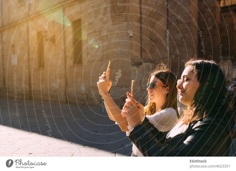 Zwei Touristinnen, die eine alte Stadt in Spanien besuchen, fotografieren ein Denkmal in Salamanca mit ihrem Handy bei Sonnenuntergang zwei Frauen Freunde