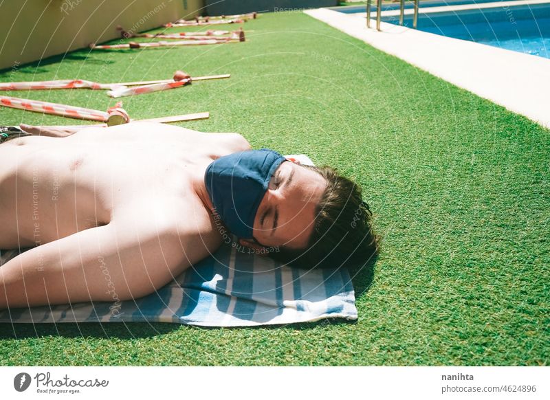 Junger Mann in einem Schwimmbad im Sommer mit einer Gesichtsmaske COVID Pandemie covid-19 Pool Mundschutz männlich Feiertage Sommerzeit ansteckend Risiko Schutz