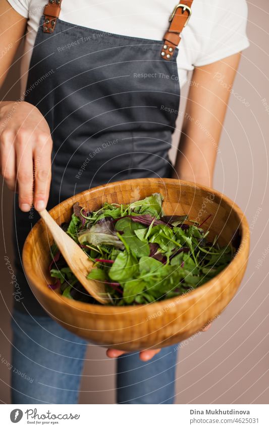 Frau Koch in einer grauen Schürze macht grünen Salat in Öko-Holz-Bambus-Schüssel in der Küche. Gesundes Essen und Ernährung, umweltbewusster Lebensstil.