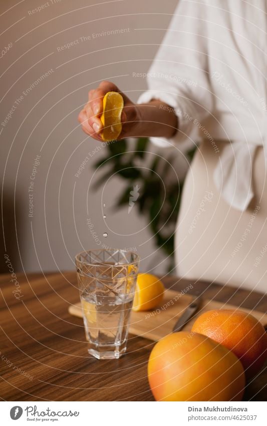 Frau presst Zitronensaft in ein Glas Wasser in der Küche zu Hause - gesunde Ernährung und Lebensstil Mineral Frische Diät modern Morgen Utensil Pflege