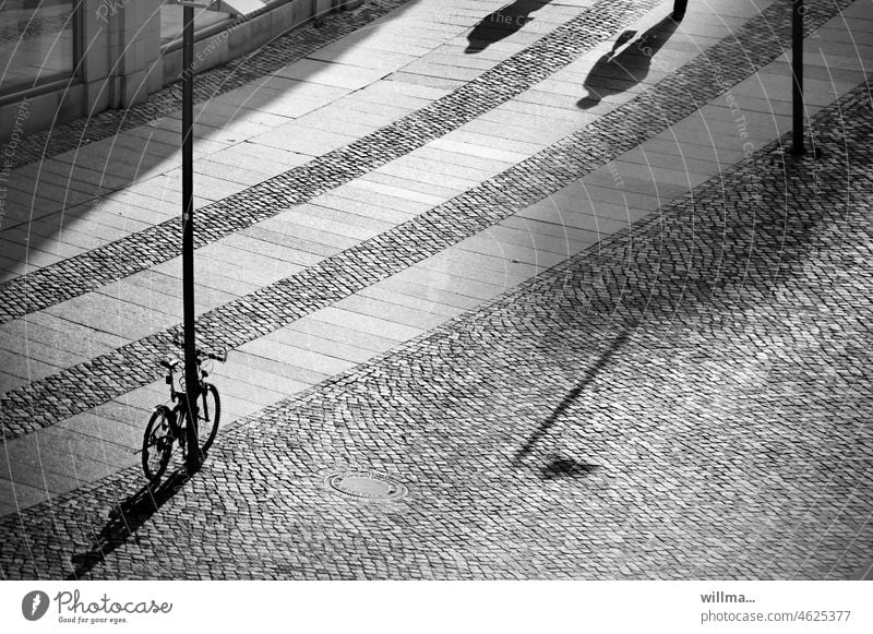 Stadtpflaster. Ein Fahrrrad und zwei Fremde. Wegweisender Laternenschatten. Fahrrad Schatten urban Platz gepflastert Personen