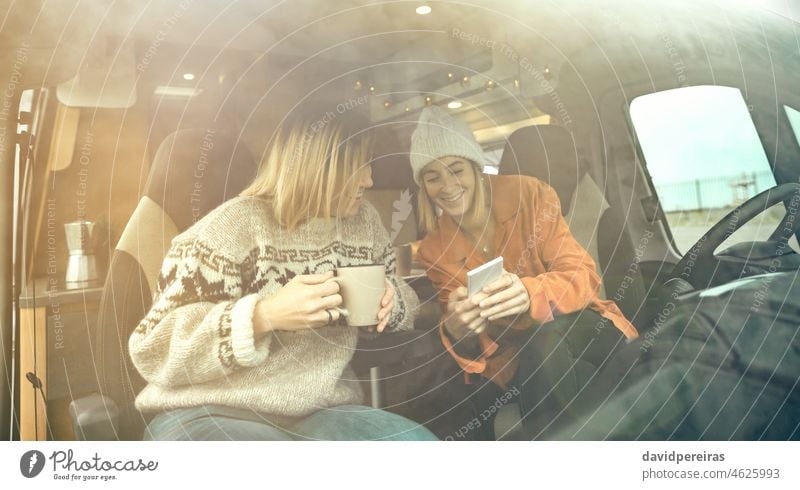 Lachende, mobil aussehende Frauen auf dem Vordersitz eines Wohnmobils Glück Spaß trinken Kaffee Blick Mobile Textfreiraum durch die Windschutzscheibe Winter