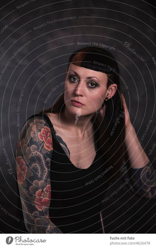 Porträt einer Frau auf dunklem Hintergrund Blick in die Kamera tattoo tätowiertes Mädchen feminin Farbfoto Tattoo Junge Frau Piercing schön authentisch