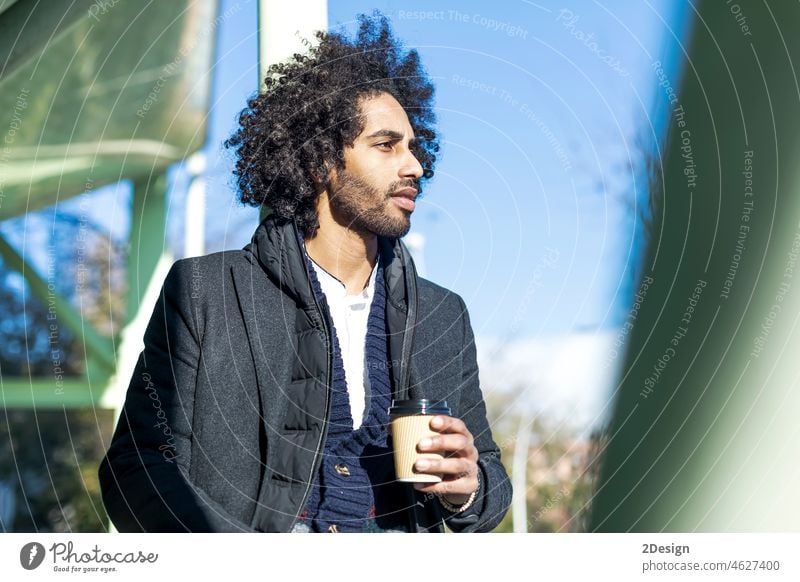 Hübscher moderner afrikanischer Amerikaner mit Bart, der lächelnd auf der Straße steht und eine Tasse Kaffee zum Mitnehmen trinkt Afro-Look männlich Lächeln
