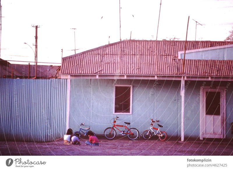 Drei Kinder mit drei Rädern sitzen auf der Erde vor einem Haus in Südamerika südamerika Kindheit Freunde freizeit spielen Kinderspiel Spielplatz Fahrrad 3