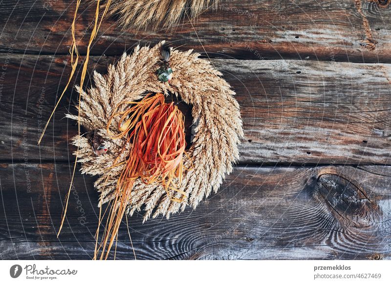 Kranz aus goldenen Ähren, getrockneten Blumen und Kräutern, gebunden mit rotem Band, an einer Holzwand Totenkranz Weizen Ohr Kraut rustikal