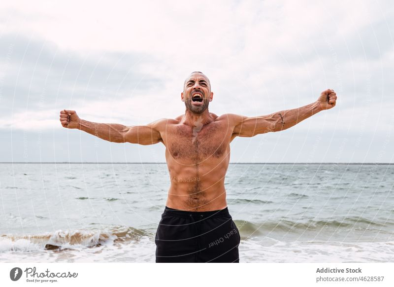Mann ohne Hemd mit ausgebreiteten Armen am Strand nackter Torso MEER Training Wasser Ufer Gesunder Lebensstil Wohlbefinden sportlich muskulös männlich schreien