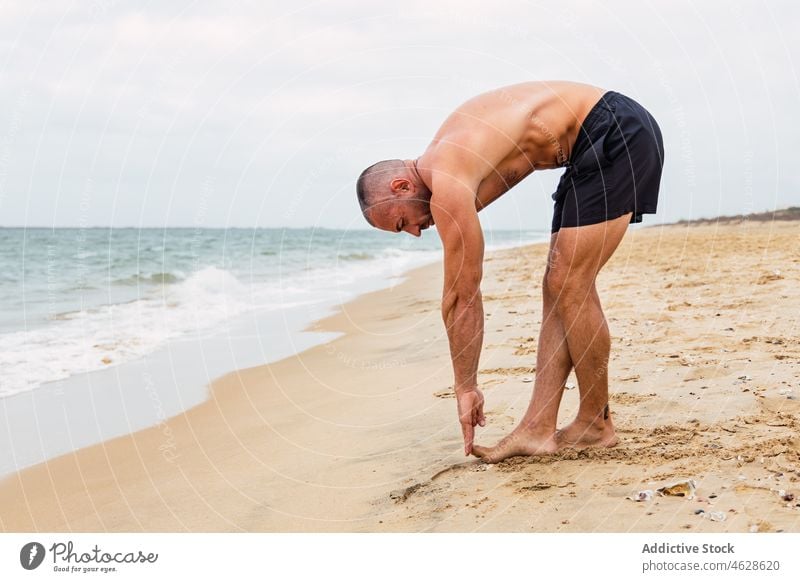 Hemdloser Mann, der sich am Strand streckt und nach vorne beugt ohne Hemd MEER Training Wasser Ufer Gesunder Lebensstil Übung Wegbiegung üben sportlich