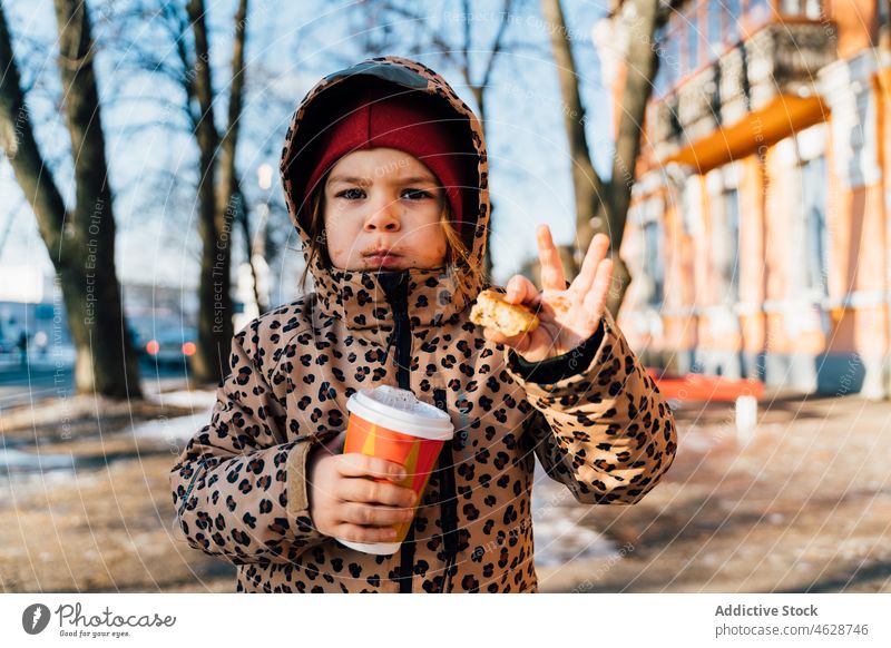 Nettes Mädchen mit Getränk zum Mitnehmen an einem Wintertag Kind Keks Imbissbude Heißgetränk Straße Großstadt kalt Kindheit Dessert trinken Oberbekleidung