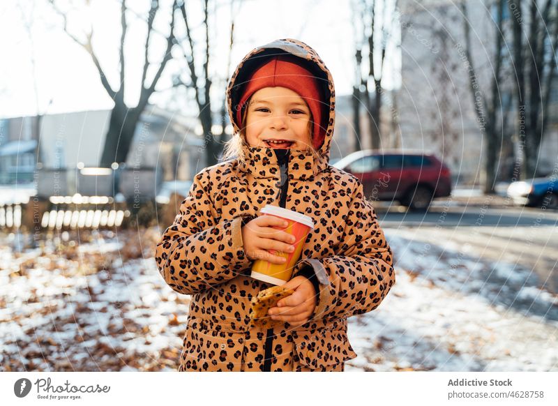 Nettes Mädchen mit Getränk zum Mitnehmen an einem Wintertag Kind Keks Imbissbude Heißgetränk Straße Großstadt kalt Kindheit Dessert trinken Lächeln