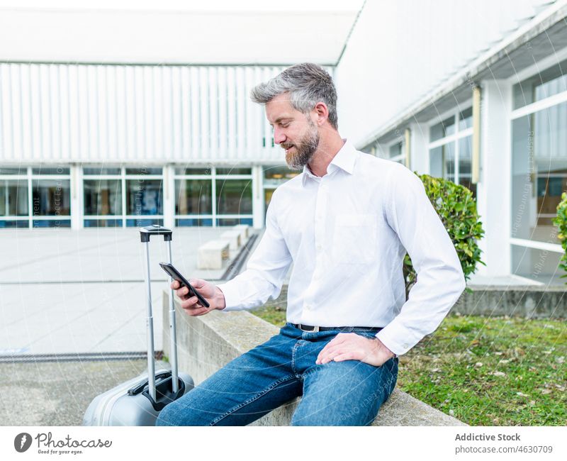 Mann surft mit Smartphone in der Nähe des Koffers Browsen online Textnachricht Gepäck Ausflug Straße Großstadt Reisender Funktelefon reisen Gebäude