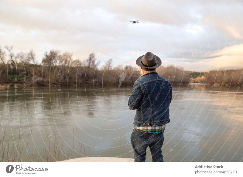 Männlicher Reisender, der eine Drohne am Seeufer fernsteuert Mann Wanderer Dröhnen Apparatur Wald Natur männlich Vollbart Sonnenuntergang Video Kontrolle