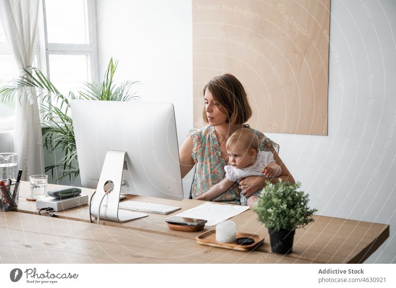 Frau mit Baby beim Surfen am Computer Mutter Mutterschaft Säuglingsalter freiberuflich Arbeit abgelegen Arbeitsplatz heimwärts Beruf Job Papier beschäftigt