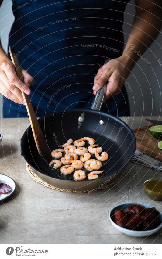 Anonymer Mann brät Shrimps in der Pfanne Granele braten Bratpfanne Koch kulinarisch Küche Bestandteil Meeresfrüchte Rezept roh Küchenchef vorbereiten