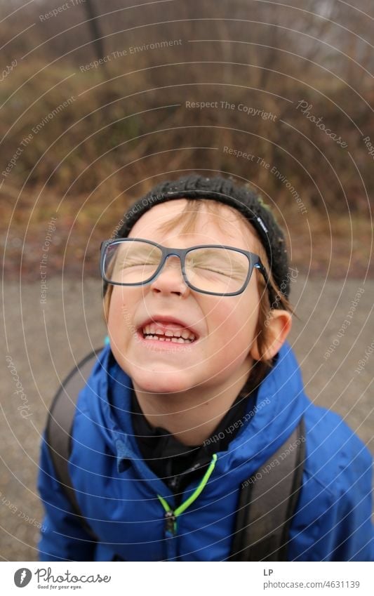 Kind mit Brille, das mit geschlossenen Augen in die Kamera schaut und die Zähne zeigt Ausdauer Hemmungslosigkeit Verachtung Verbitterung trotzig