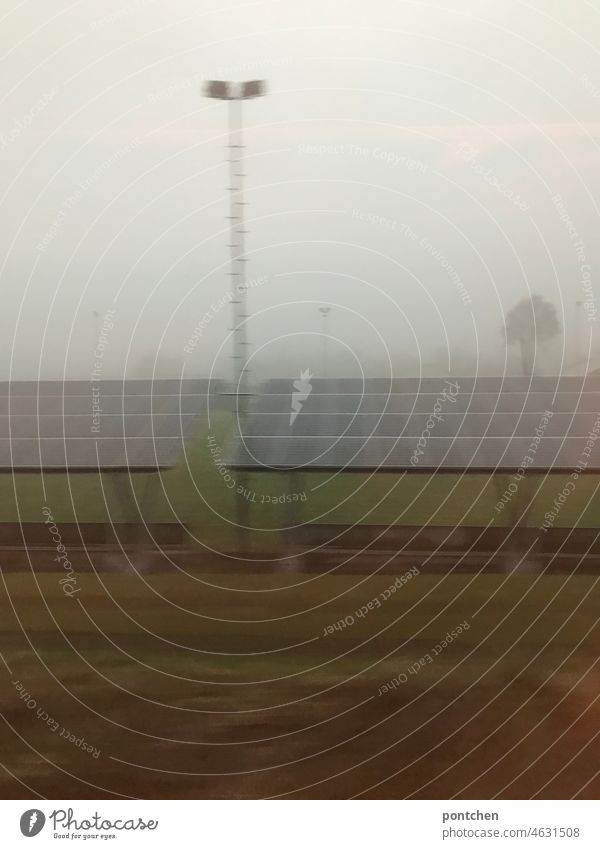 ein fußballstadion mit flutlichtmast im nebel durchs zugfenster gesehen. futlichtmasten volkssport fußballverein zugfahrt Stadion Sportstätten Fußballplatz