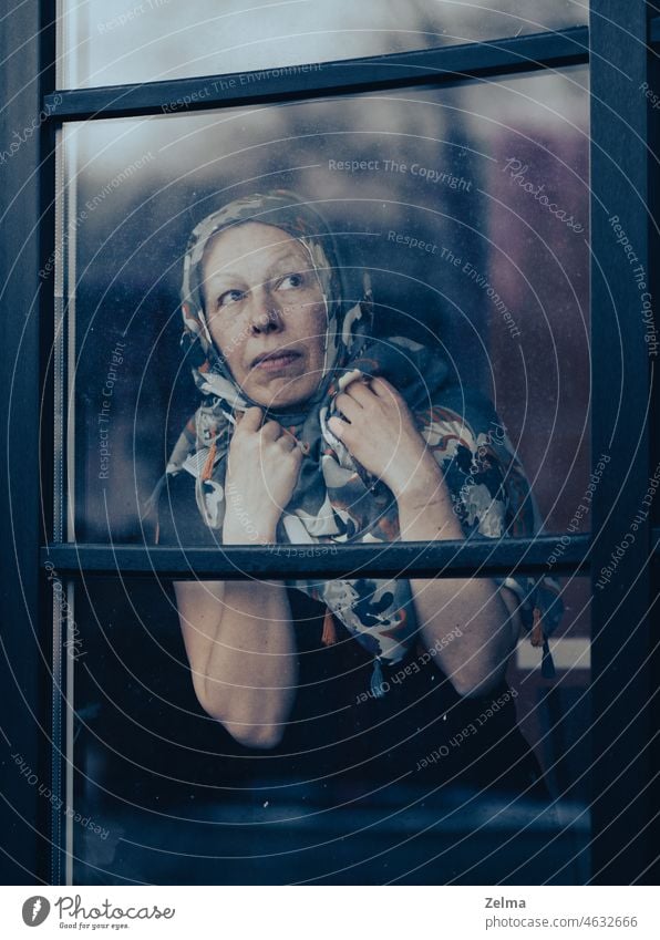 Traurige reife Frau mit Schorf auf dem Kopf hinter schmutzigem Fensterglas stehend mittleren Alters älter Aussehen durch hinten dreckig Glas Schal Gesicht