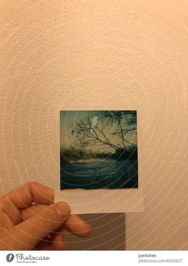 Hand hält ein Polaroid vor eine Wand. Naturaufnahme, Fluss. blau inn fluss schönes wetter halten wand schatten zeigen rahmen landschaft Außenaufnahme Himmel