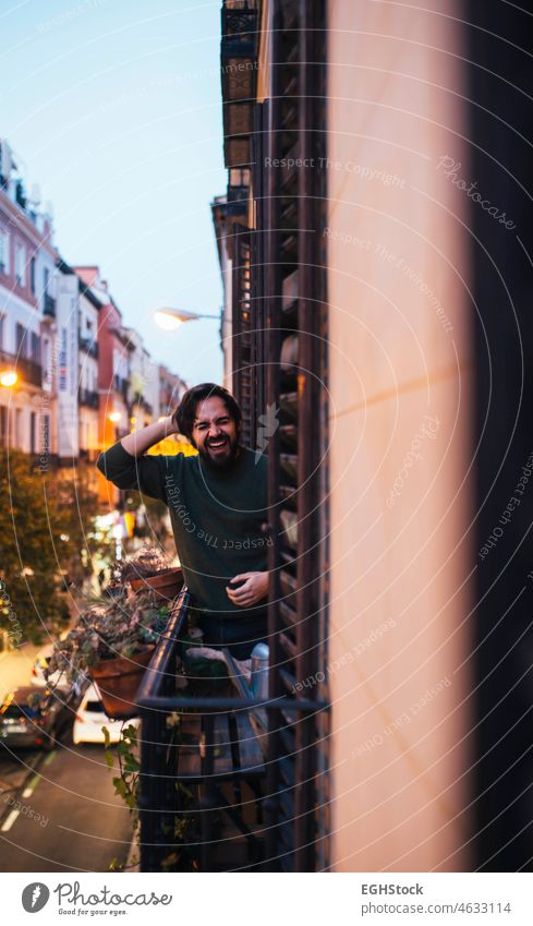 Fröhlicher, lässiger junger Mann, der auf dem Balkon einer typischen Madrider Gebäudefassade auf der Straße lacht Glück Lachen Vibrationen gut Zentrum alt