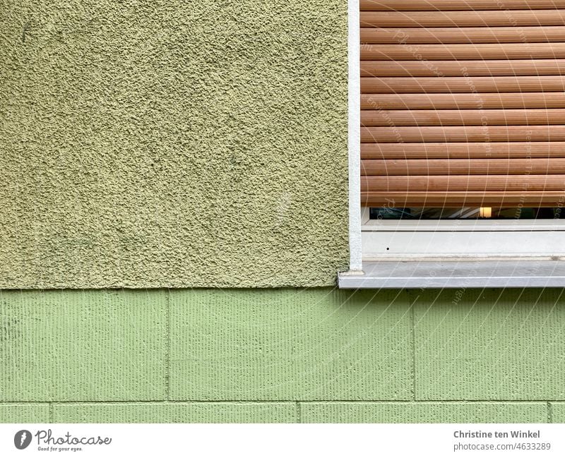 Nahaufnahme eines grünen Hauses mit einem weißen Fenster und braunem, fast geschlossenen Rollladen Fassade grüne Fassade Wohnhaus Putzfassade verputzt Stadt