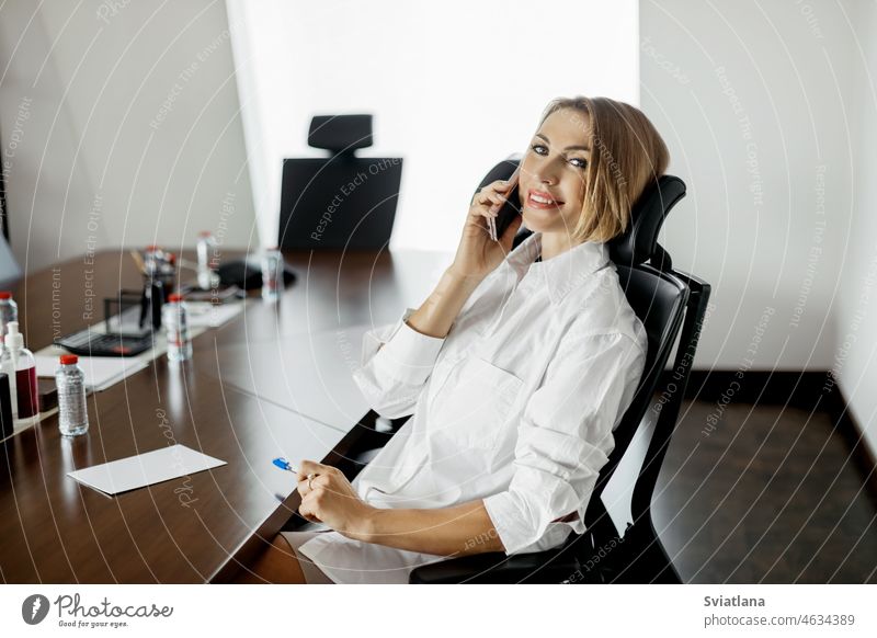 Eine Geschäftsfrau telefoniert an einem Schreibtisch im Büro sitzend Telefon Mobile Blick Lächeln Frau Fenster modern Business Person professionell