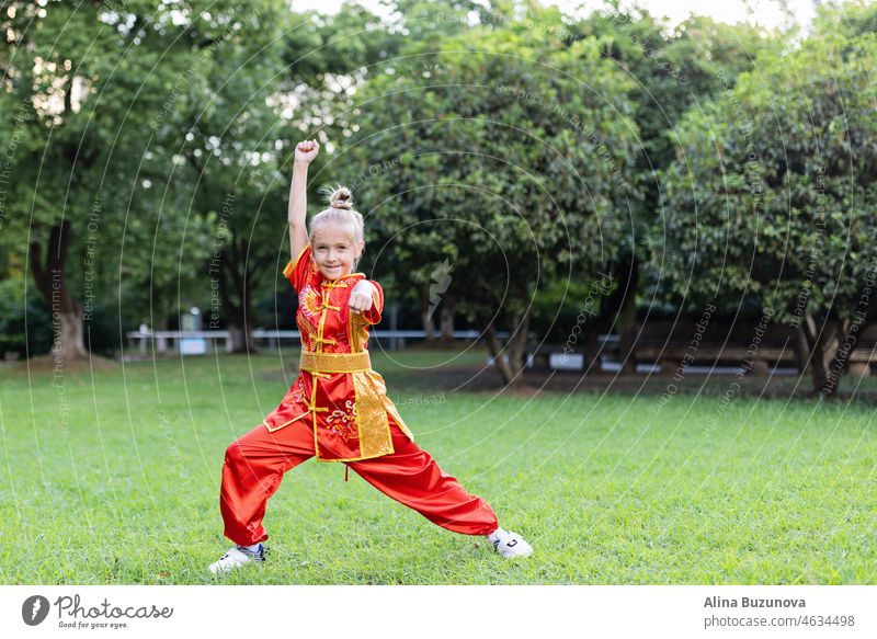 Cute kleine kaukasische Mädchen sieben Jahre alt in roten Sport Wushu Uniform Ausübung im Park am Sommertag. Lifestyle-Porträt von Kung-Fu-Kämpferin Kind Athleten