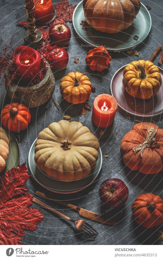 Herbststilleben mit verschiedenen bunten Kürbissen, Kerzen, Tellern, Besteck auf dunklem Küchentisch. Stillleben farbenfroh Platten Dekoration & Verzierung
