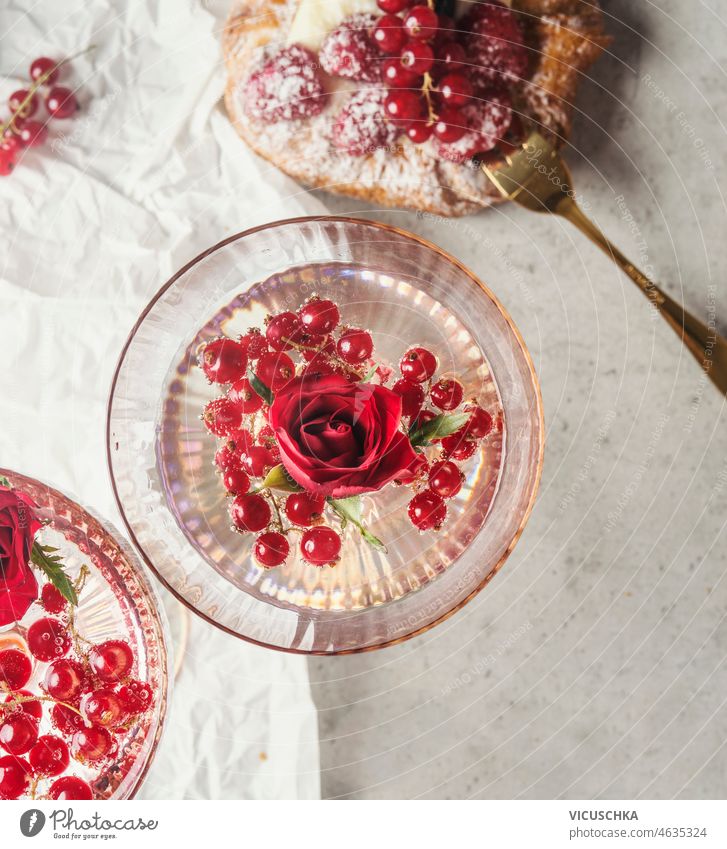 Champagnerglas mit Rosenblüten und roten Johannisbeeren auf weißem Hintergrund mit Beerenkuchen. Glas Roséwein Blütenblatt rote Johannisbeeren auf Weiß Torte