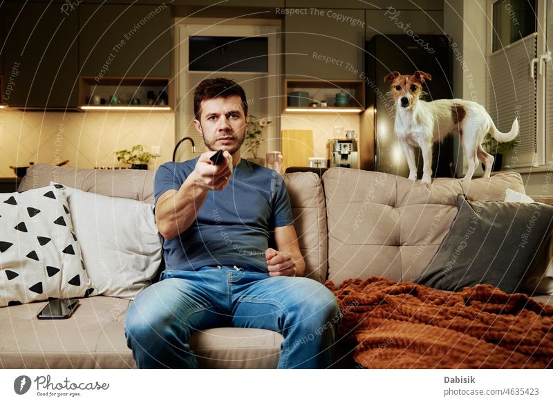 Mann benutzt Fernbedienung, um fernzusehen verwenden zuschauend FERNSEHER Sofa Wohnzimmer Schalter Hund Liege im Innenbereich ruhen Tier Haustier LAZY Freizeit