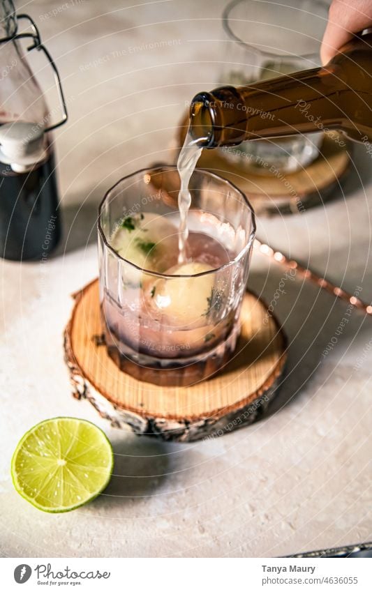 Einschenken von Bier in ein klares Cocktailglas mit Eiswürfeln und Limette Gesundheit Frische grün erfrischend Erfrischung Getränk Limonade Bourbon Whiskey