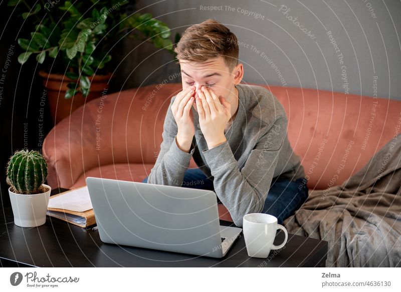 Ich fühle mich müde. Frustrierter junger Mann, der erschöpft aussieht und sein Gesicht mit den Händen bedeckt, während er an seinem Laptop sitzt und zu Hause arbeitet