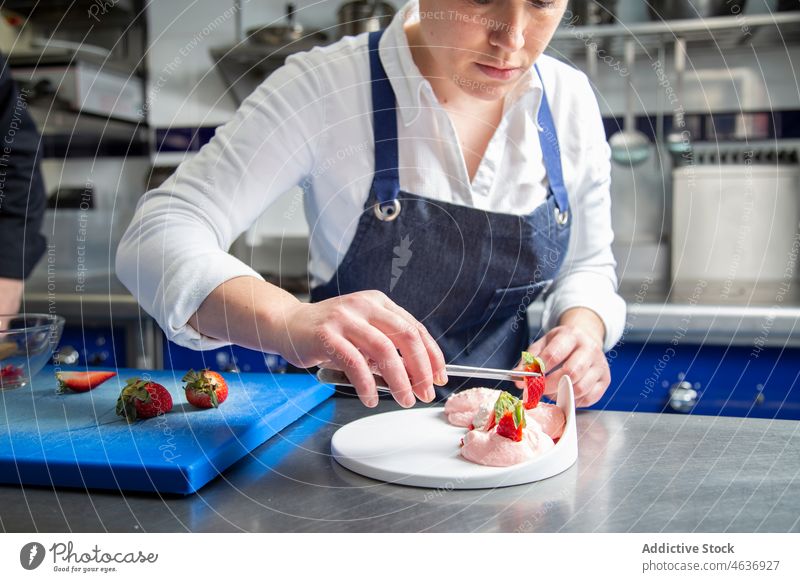 Köchin garniert Dessert mit Erdbeere Frau Küchenchef Garnierung Erdbeeren Sahne gepeitscht Restaurant Koch Lebensmittel vorbereiten Schürze frisch Pinzette