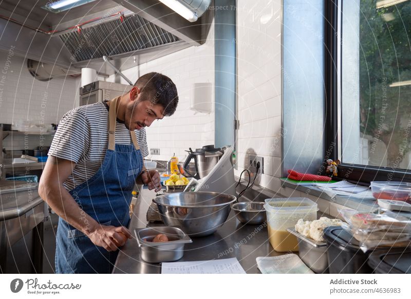 Bärtiger ethnischer Koch bricht ein Ei während der Arbeit in der Küche auf Mann Pause Bestandteil kulinarisch Lebensmittel vorbereiten Konzentration Job