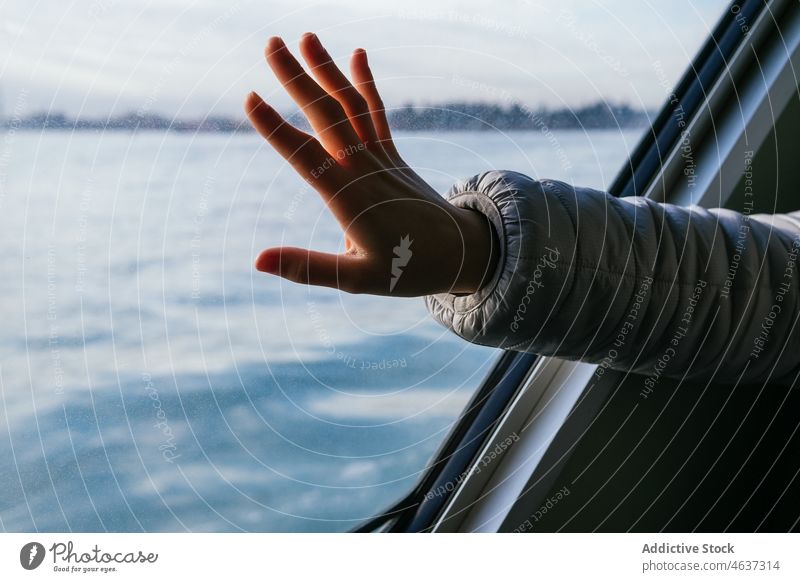 Crop-Touristin berührt das Fenster im Boot Frau berühren Kreuzfahrt Ausflug Fluss Reise Urlaub Tourismus Verkehr Hand Jacke warme Kleidung wolkig Himmel