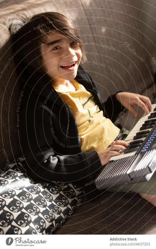 Fröhlicher ethnischer Junge spielt auf dem Keyboard Kind Synthesizer Instrument Kindheit Musical Gesang Musik spielen Melodie unterhalten Wohnzimmer heimwärts