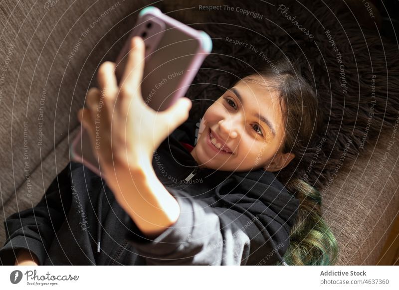 Fröhliches ethnisches Mädchen nimmt Selfie auf Couch Teenager Smartphone Selbstportrait Fotografie Liege Hobby Wohnzimmer soziale Netzwerke heimisch froh