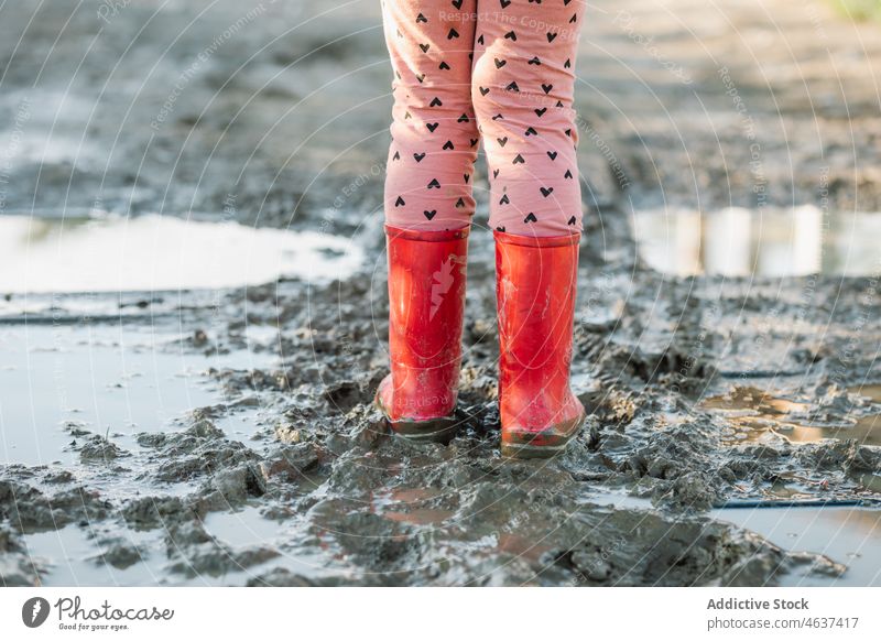 Anonymes Kind steht auf schmutzigem Boden Weg Gummistiefel Schmutz Schlamm Pfütze nass Wasser Straße Kindheit Stiefel dreckig Bürgersteig Farbe Laufsteg hell