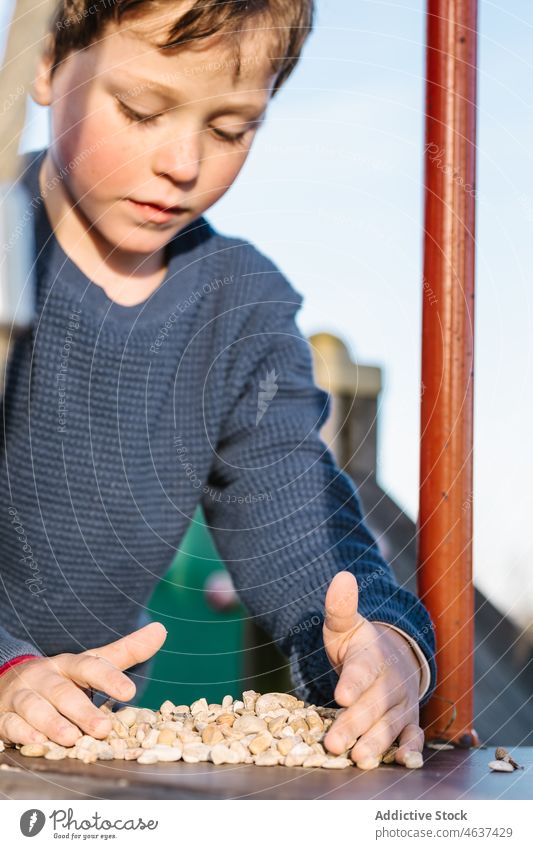 Junge spielt mit Kieselsteinen auf dem Spielplatz Kind spielen Kindheit Vergnügen spielerisch Stein Zeitvertreib Mast Metall Sommer Freizeit Erholung ruhen