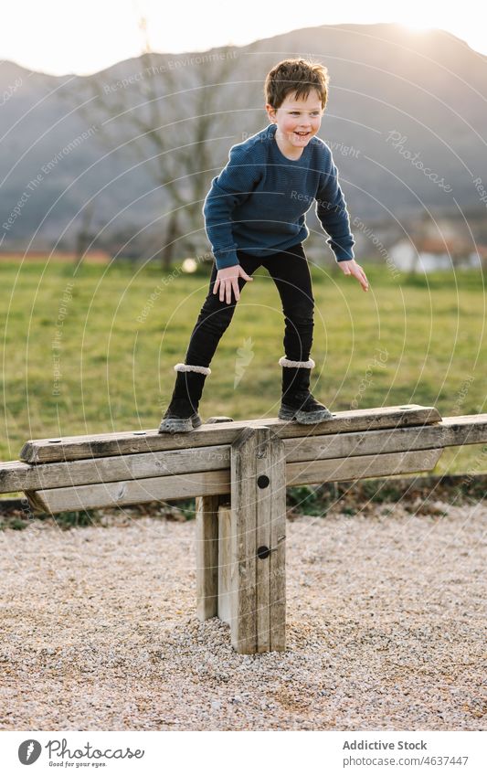 Fröhlicher Junge auf hölzerner Wippe stehend Kind Spielplatz spielen unterhalten Kindheit Vergnügen heiter Landschaft Lächeln Gleichgewicht Glück