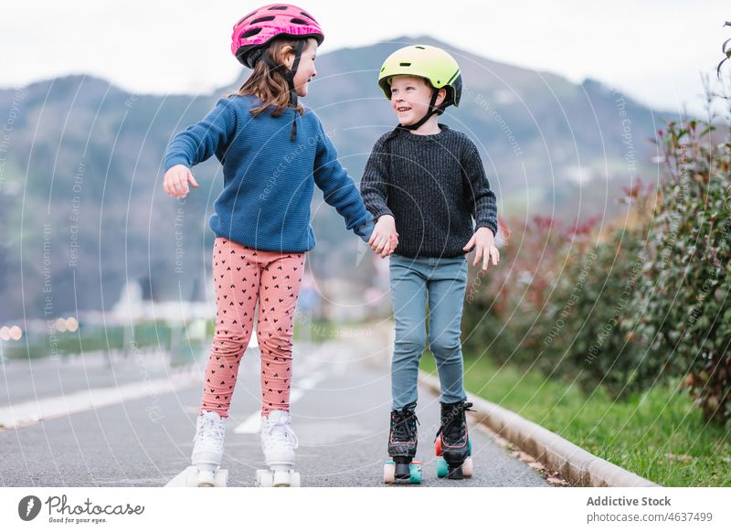 Kinder halten sich an den Händen und fahren auf Rollschuhen auf der Straße Rollerskate Mitfahrgelegenheit Hobby Kindheit Freizeit Zeit verbringen Natur