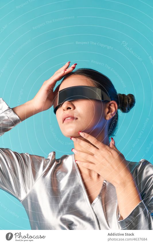 Ethnische Frau, die ihr Gesicht berührt, während sie die virtuelle Realität mit einer futuristischen Brille erlebt Gesicht berühren Virtuelle Realität Stil