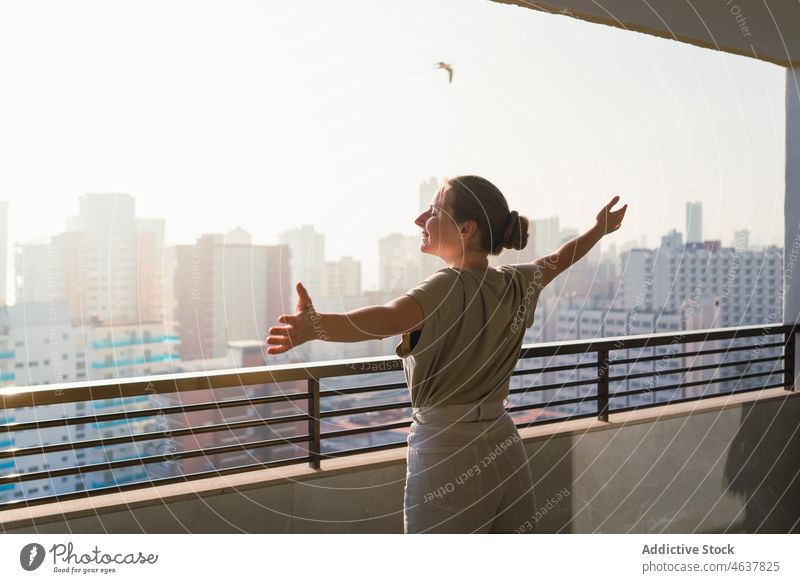 Zufriedene junge Frau genießt den sonnigen Tag auf dem Balkon mit ausgestreckten Armen Lächeln genießen Stadtbild Urlaub ausdehnen Terrasse Tourist Freude