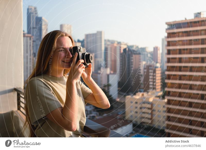 Junge Frau fotografiert die Stadt mit einer Retrokamera auf einer Terrasse fotografieren Fotoapparat Großstadt Tourist Urlaub Lächeln Feiertag Architektur