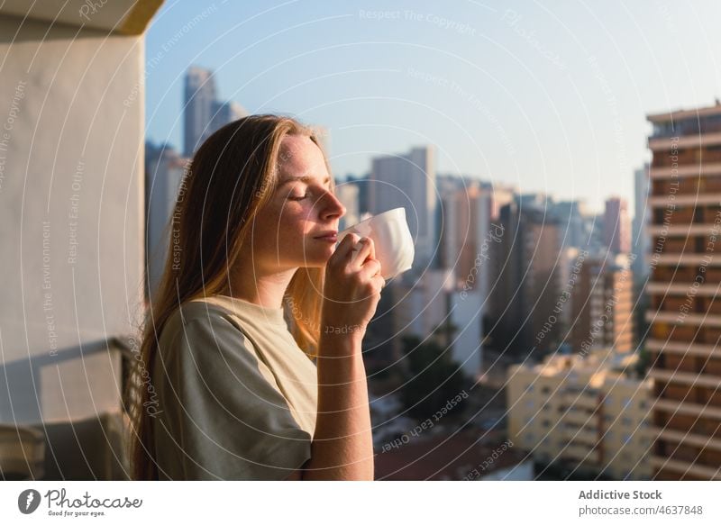Ruhige junge Frau genießt Kaffeeduft auf Balkon sonnig am Morgen trinken Terrasse Großstadt Wochenende genießen Augen geschlossen sich[Akk] entspannen friedlich