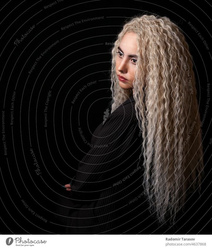 Porträt eines jungen blonden Mädchens mit langen lockigen Haaren lange Haare schwarz Hintergrund Atelier Frau schön niedlich attraktiv hübsch Glück Jugend